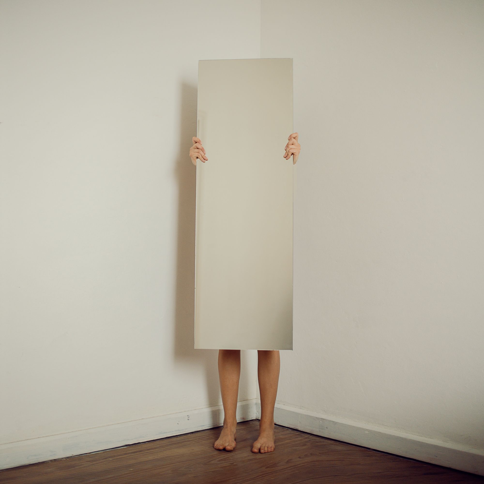 Artistic shot of a woman holding a mirror in a minimalist room, emphasizing reflection and simplicity.