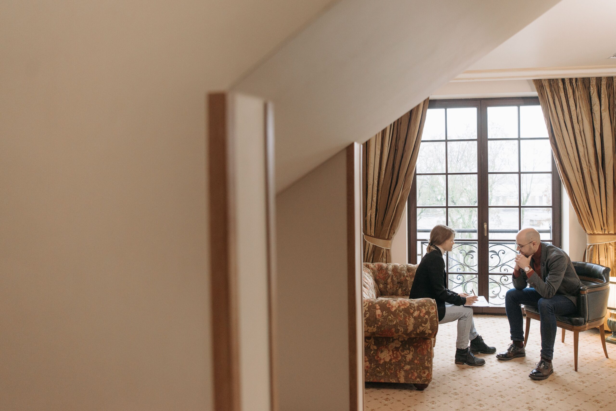 Two professionals in a serious discussion in a tastefully decorated office, featuring cozy furniture and large windows.